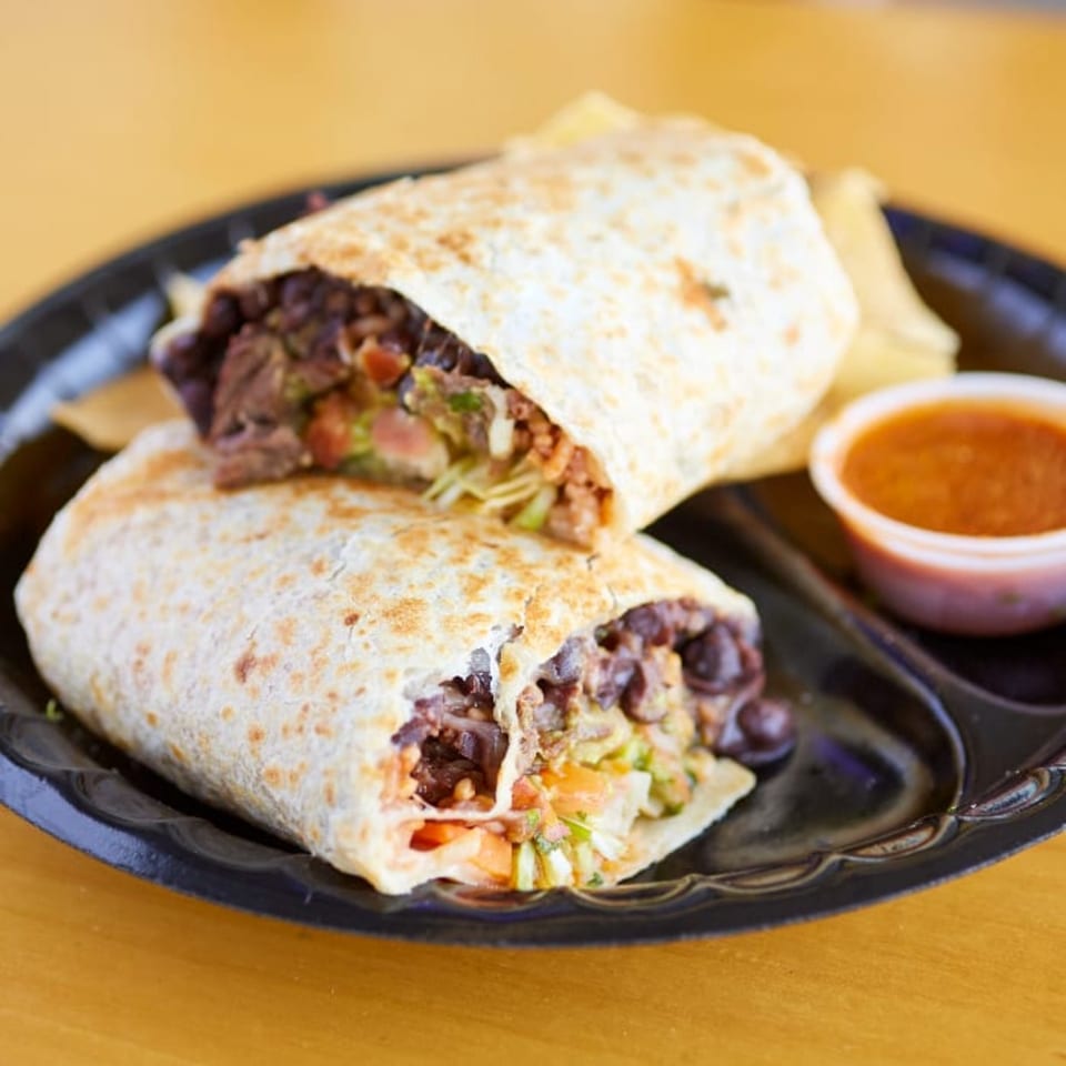 Two large burritos, cut in half to show fillings, with a side of salsa and tortilla chips.