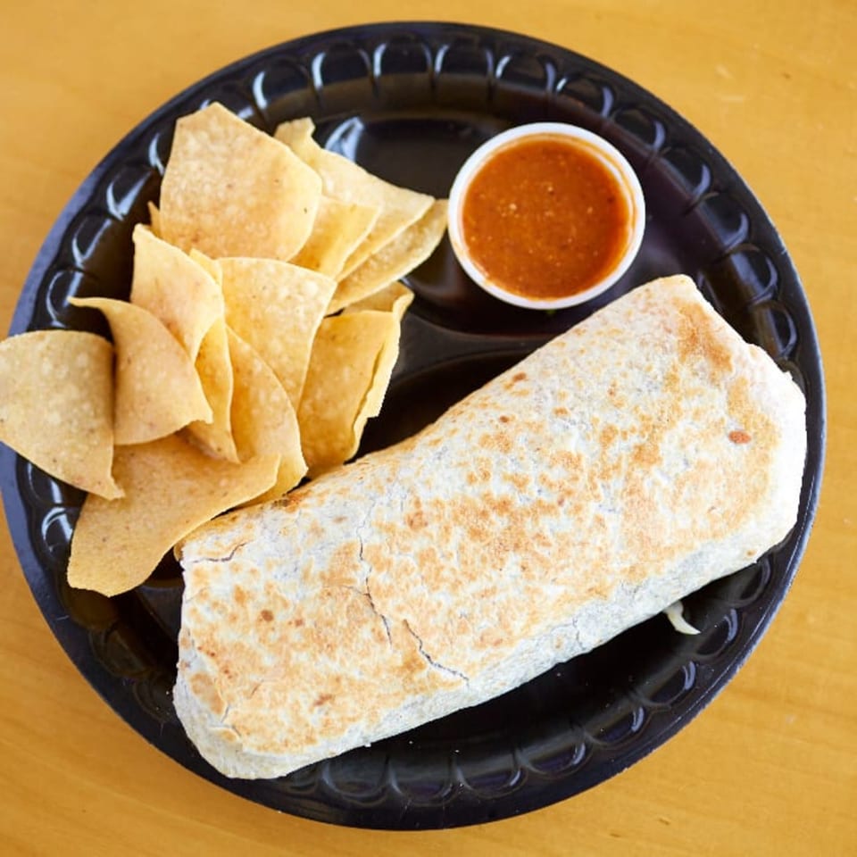 A large burrito, tortilla chips, and a side of salsa on a black plate from Pachanga Mexican Grill.