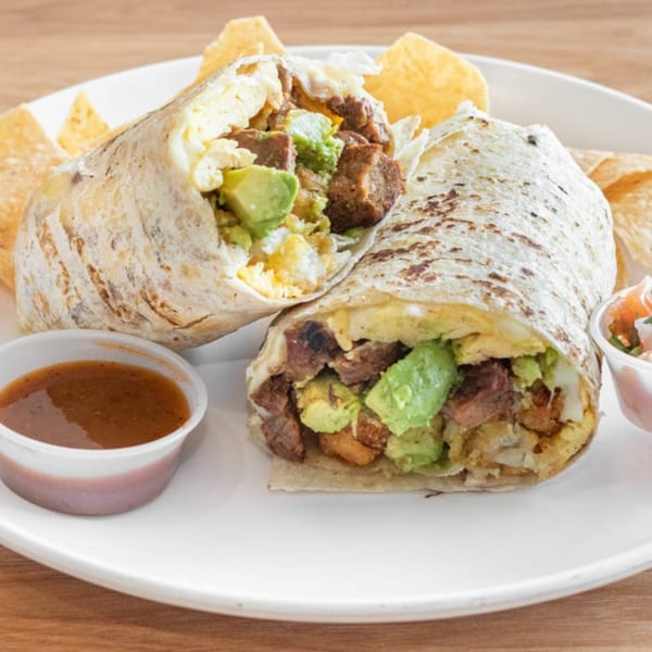 A Pachanga Mexican Grill burrito, cut in half, filled with meat, avocado, and eggs, served with chips and salsa.